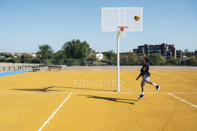 Jovem jogando na quadra de basquete ao ar livre . — Fotografia de Stock