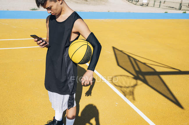 Basketballer nutzt Smartphone als Ruhepause nach Trainingseinheit. — Stockfoto