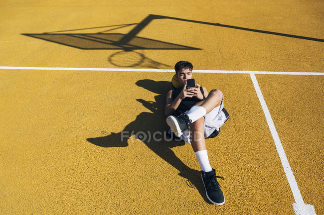 Мужчина баскетболист с помощью смартфона, лежащий на желтой корте после тренировки
. — стоковое фото