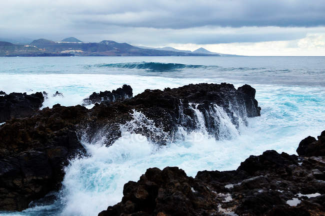Ondas azules del océano con textura de espuma blanca contra rocas. - foto de stock
