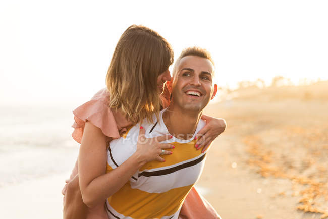 Cheerful male giving piggyback ride to smiling female on resort — Stock Photo