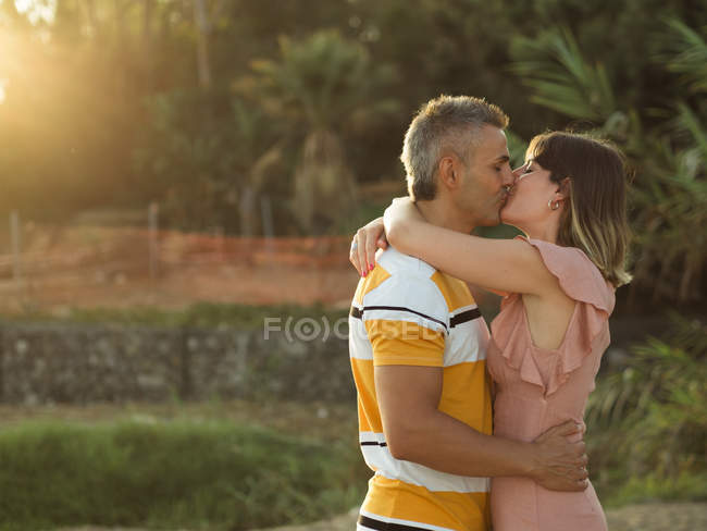 Mid adult couple embracing and kissing outdoors in backlit — Stock Photo