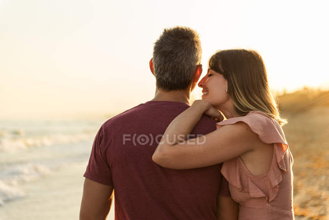Adult woman leaning on man while standing on beach near waving sea — Stock Photo
