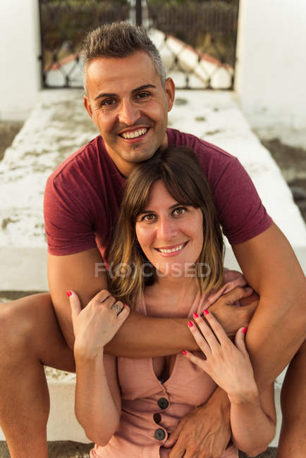 Fröhliche erwachsene Mann und Frau lächelnd und umarmend, während sie auf Stufen vor dem Gebäude sitzen — Stockfoto