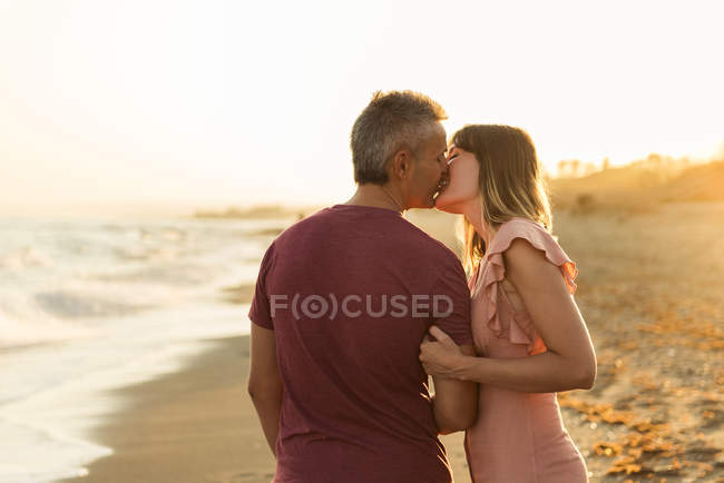 Adulto homem beijando mulher na praia perto do mar ondulando e descansando juntos — Fotografia de Stock