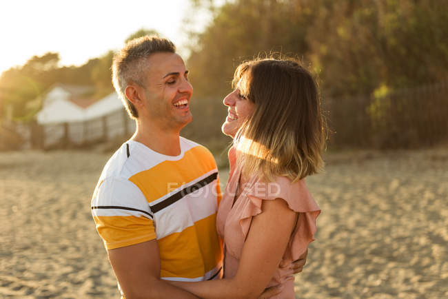 Excited adult man and woman laughing and embracing each other while having fun on sandy shore on resort — Stock Photo