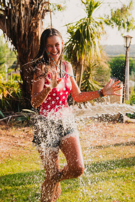 Jeune fille excitée riant et jouant avec un jet d'eau propre tout en s'amusant dans le jardin le jour ensoleillé — Photo de stock