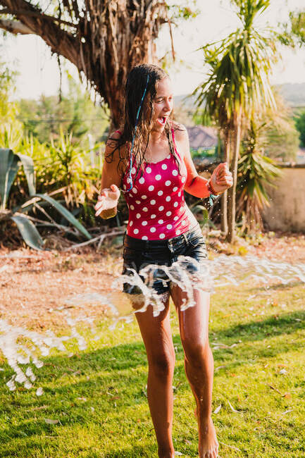 Garota adolescente excitada rindo e brincando com jato de água limpa enquanto se diverte no jardim no dia ensolarado — Fotografia de Stock
