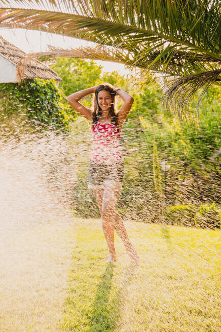 Eccitato teen girl ridendo e giocando con getto d'acqua pulita mentre si diverte in giardino nella giornata di sole — Foto stock
