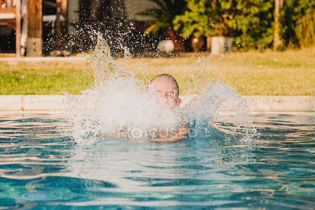 Aufgeregtes Mädchen in Höschen hebt die Hände und schreit, während es im Hof ins Pool-Wasser springt — Stockfoto