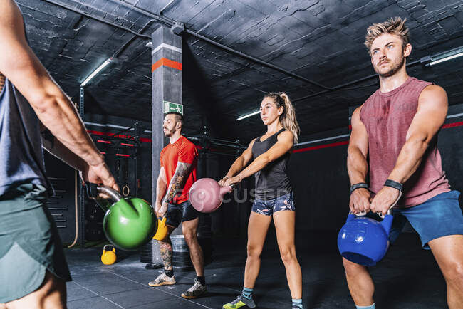 Side view of athletic strong fellows doing workout with weight in gym - foto de stock