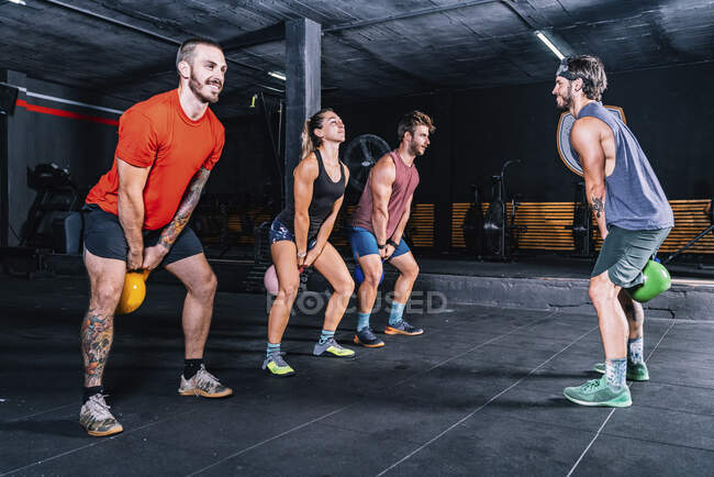 Muscular fellows with coach lifting up kettle bells while functional training in contemporary health club — Stock Photo