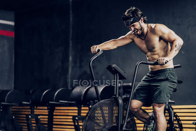 Forte homem formação em bicicleta de exercício contemporânea no clube desportivo — Fotografia de Stock