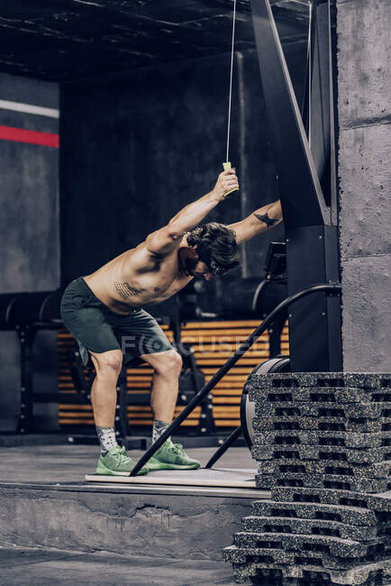 Мускулистый человек делает тренировку на верхней части тела машины в современном спортивном клубе — стоковое фото