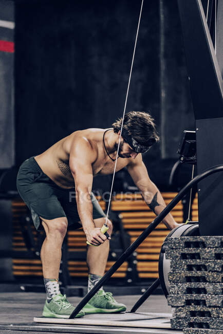 Мускулистый человек делает тренировку на верхней части тела машины в современном спортивном клубе — стоковое фото