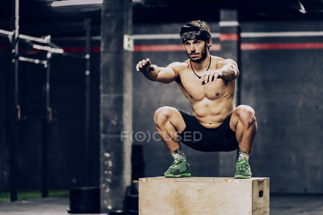 Athletic man jumping on box to improve stamina in gym — Stock Photo