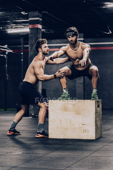 Спортивний тренер стрибає на коробці і допомагає клієнту покращити витривалість у тренажерному залі — стокове фото