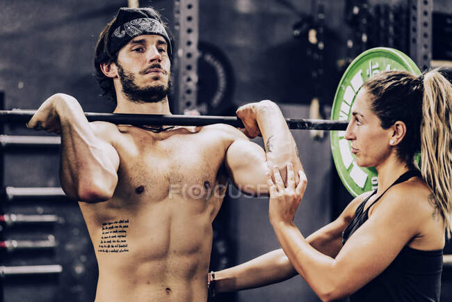 Strong coach in sportswear helping athletic client and doing barbell workout in modern gym — Stock Photo