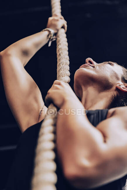 De baixo mulher muscular escalando corda e olhando para cima no fundo preto — Fotografia de Stock