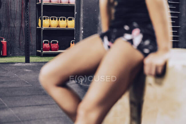 Crop cansado fêmea em sportswear relaxante no ginásio em fundo borrado — Fotografia de Stock