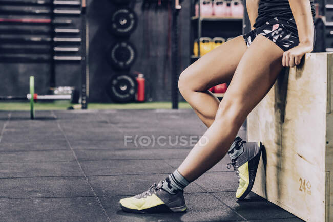 Обрізати втомлену жінку в спортивному одязі, розслабляючись у спортзалі на розмитому фоні — стокове фото