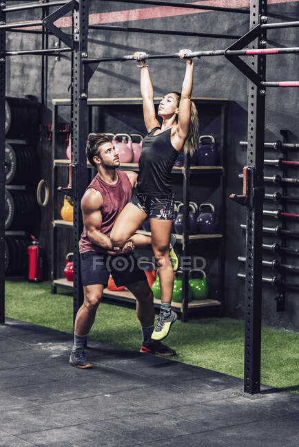 Starker Trainer in Sportbekleidung hilft athletischen Kunden und macht Klimmzug-Workout in modernem Fitnessstudio — Stockfoto