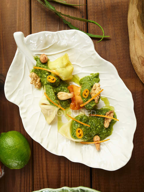 Верхний вид макаронных пельменей с травяным соусом и орехами на листовидной тарелке на деревянном столе — стоковое фото
