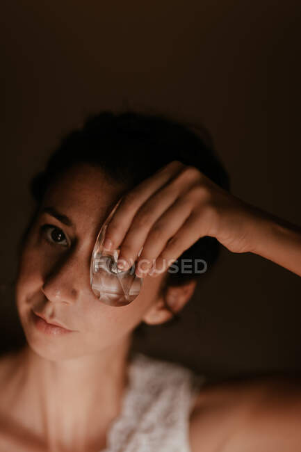 Jovem mulher olhando para a câmera através de jóias transparentes no quarto escuro — Fotografia de Stock