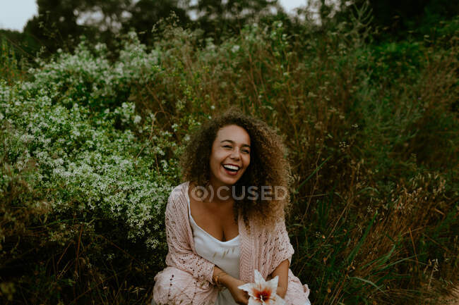 Улыбающаяся женщина касается цветка в лесу — стоковое фото