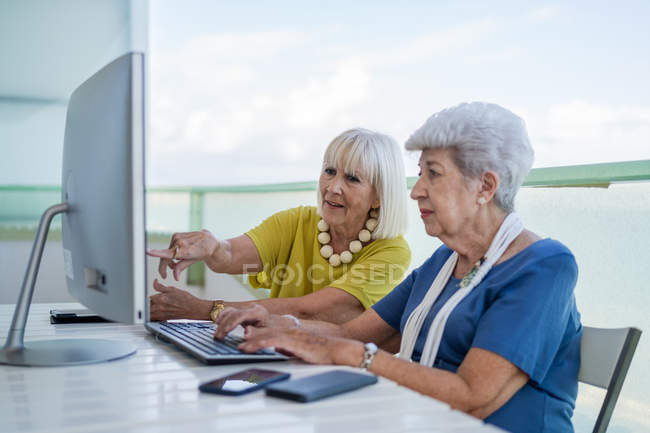 Elegantes viejos amigos sentados en la mesa con computadora en el balcón en el resort - foto de stock