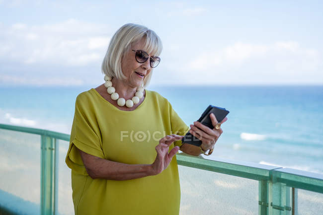 Stilvolle Seniorin surft auf dem Smartphone in den sozialen Medien und schaut vom Balkon weg — Stockfoto