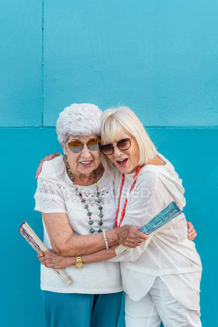 Positive trendy grey-haired women with big color hand fans hugging — Stock Photo
