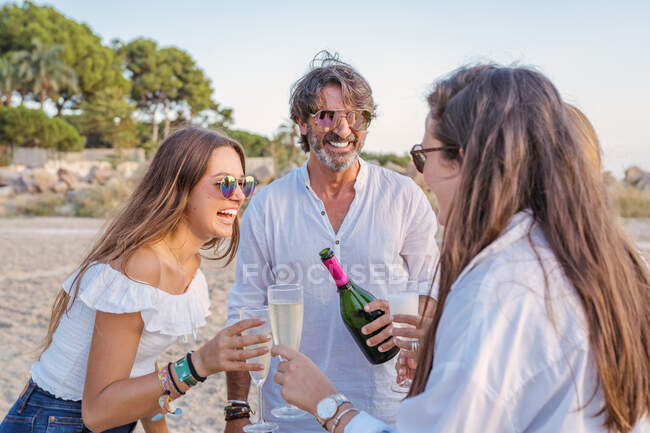 Pai e filhas jovens batendo copos de vinho e rindo enquanto comemoram a reunião de família à noite no resort — Fotografia de Stock