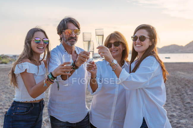 Allegro genitori maturi e giovani figlie clinking bicchieri di vino e ridere mentre si celebra riunione di famiglia in serata sul resort — Foto stock
