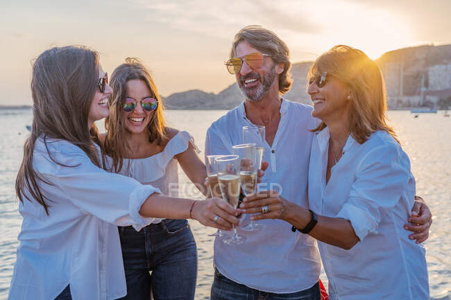 Pais maduros alegres e filhas jovens batendo copos de vinho e rindo enquanto comemoram o reencontro familiar à noite no resort — Fotografia de Stock