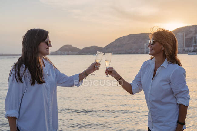 Mutter und kleine Tochter klimpern mit Weingläsern und lachen, während sie abends im Resort ein Familientreffen feiern — Stockfoto