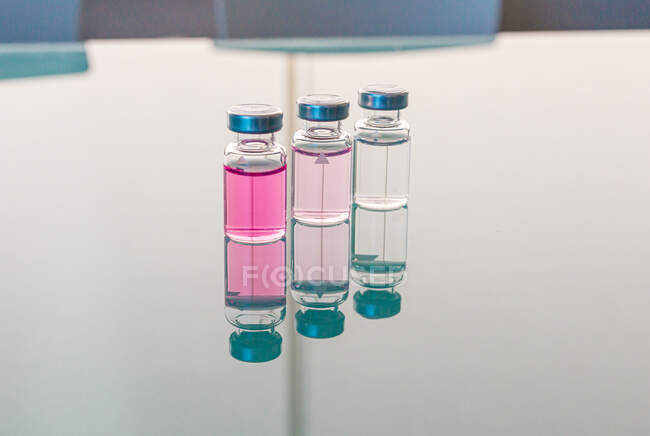Fila de frascos transparentes con líquido rosa reflejado en la mesa de cristal en laboratorio biológico durante el día - foto de stock