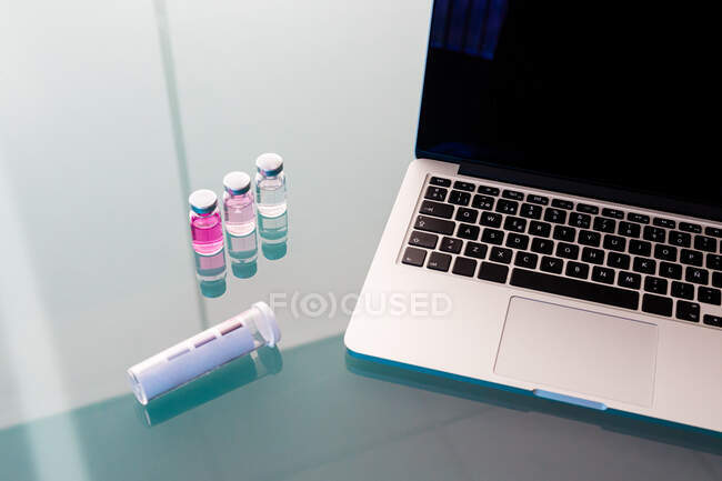 Flacons en verre d'en haut avec liquide rose et tube vide sur la table par ordinateur portable avec écran noir en laboratoire — Photo de stock