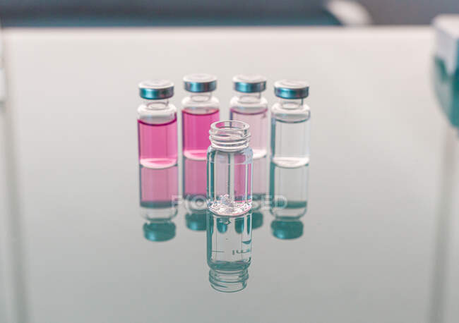 Viales con muestras científicas dispuestas sobre mesa de vidrio - foto de stock