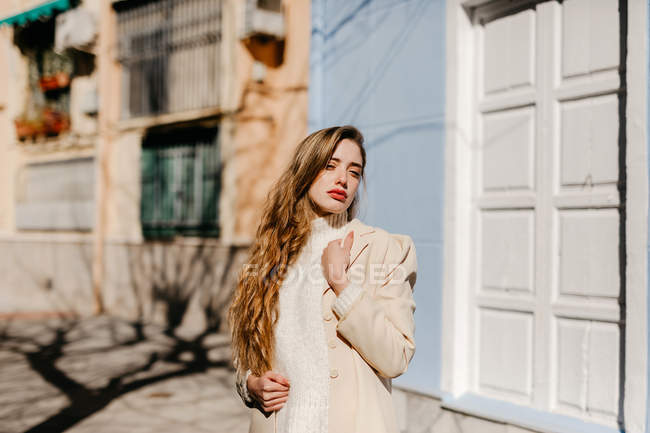 Young lady in elegant blouse looking away while standing near building on street in blurred background — Stock Photo