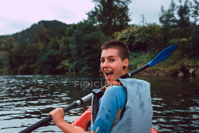 Vista posterior de la deportista emocionada mirando por encima del hombro mientras acolcha en canoa roja en el río Sella en España - foto de stock