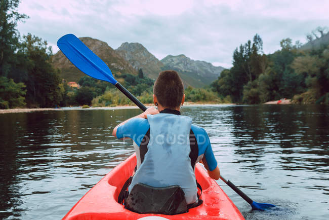 Vista posterior de la joven mujer deportiva acolchado en canoa roja en el río Sella en España - foto de stock