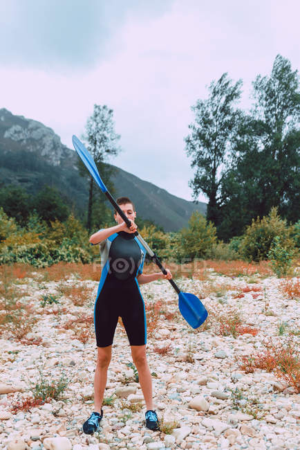 Sportive woman in wetsuit training with paddle while standing on bank of Sella river in Spain — Stock Photo