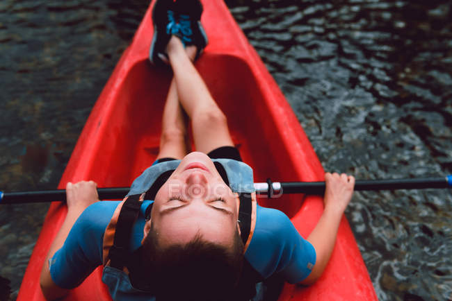 Vista de ángulo alto de la deportista sentada en canoa roja con los ojos cerrados en el agua del río - foto de stock
