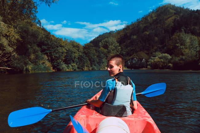 Visão traseira da esportista olhando sobre o ombro almofadado em canoa vermelha no rio Sella, na Espanha — Fotografia de Stock