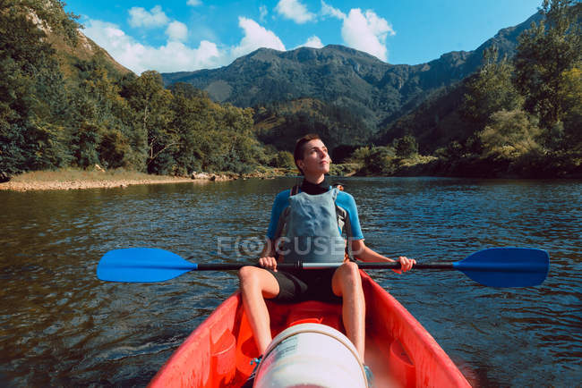 Mujer deportiva descansando en canoa roja y mirando hacia arriba en declive del río Sella en España - foto de stock