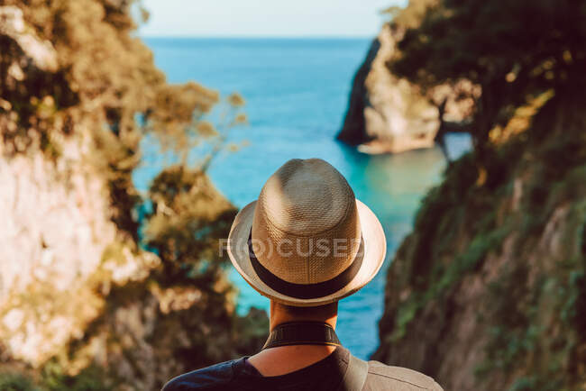 Rückenansicht einer Frau mit Hut, die an einem Holzgeländer steht und einen atemberaubenden Blick auf das Meer und die Klippen in Ribadedeva Asturias genießt — Stockfoto