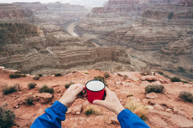 Vue recadrée des mains de l'homme savourant une boisson tout en ayant une pause au bord des falaises dans le canyon aux États-Unis — Photo de stock