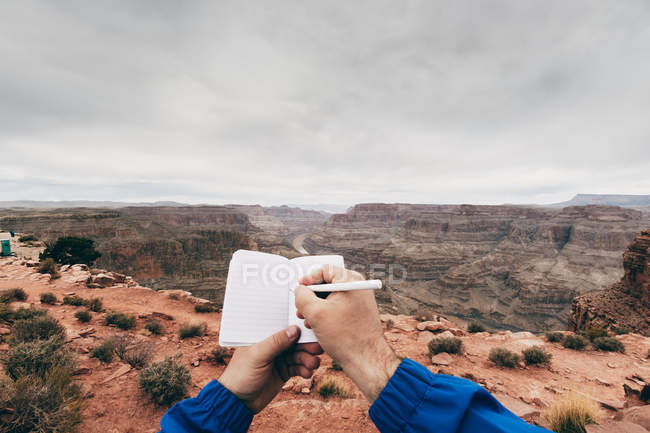 Cropped view of hands of man making notes in diary while resting at edge of cliffs in canyon in USA — Stock Photo