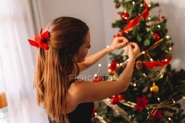 Happy young woman decorating Christmas tree with balls at home. — Stock Photo